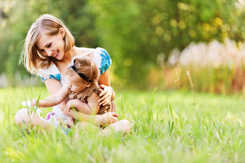 A mom playing in the grass with her young daughter.