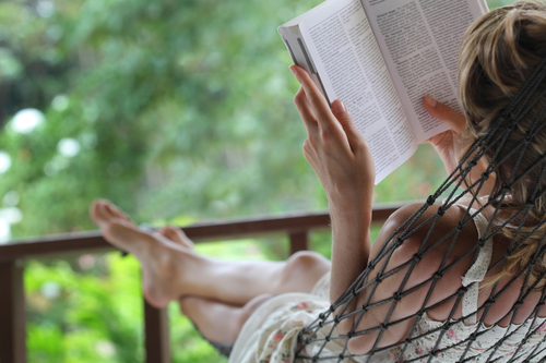 A woman relaxing in a hammock, reading a book.