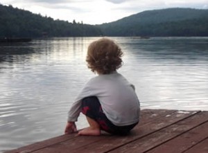 A child crouched on a dock by a lake.