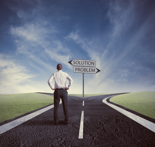 A man at a crossroad with signs pointing in opposite directions, saying solution and problem.