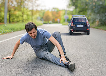 Injured man on road in front of a running away car