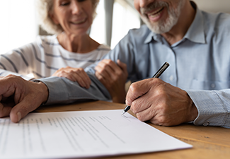 Husband and Wife Sit at Desk Sign Estate Planning Contract