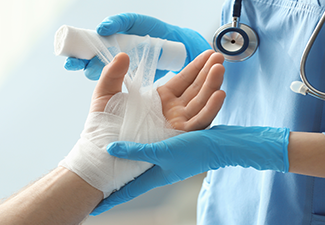 Medical assistant applying bandage onto patient's hand in clinic.