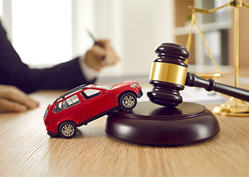 Small car model on wooden desk with judge's hammer