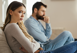 Young Woman Sitting on Sofa at Home and Ignoring Her Husband