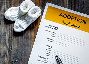 Adoption application near baby sock on dark wooden table