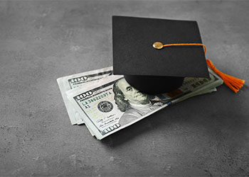 Graduation hat and dollar banknotes on table