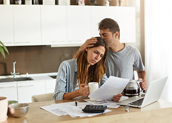 Husband Consoling Frustrated Wife in kitchen looking at financial document