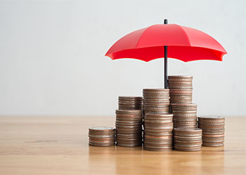 Stacked coins is protected by red umbrella on wooden table