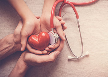 Child and adult holding red heart with stethoscope