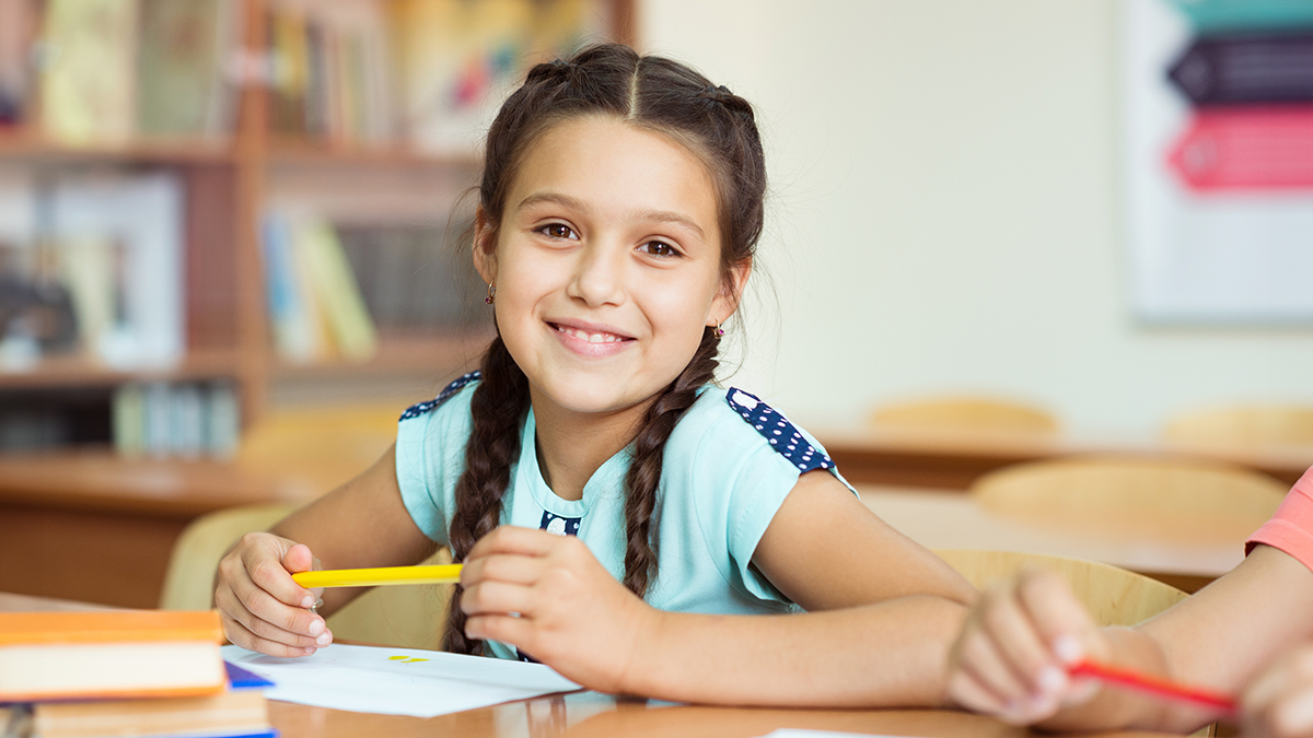 A girl with her hair in braids, sitting in a school desk.