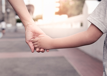 Parent holds the hand of a small boy in street