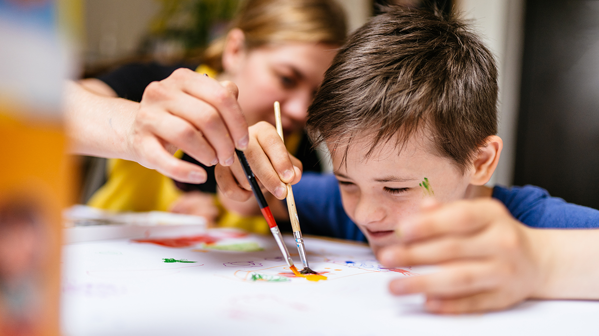 A special needs boy painting with his mom.