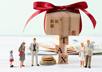 House model wrapped in red ribbon atop "TAX" wooden cubes