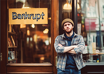 Small shop owner standing Infront of door with Bankrupt sign