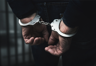 Arrested man with cuffed hands behind prison bars