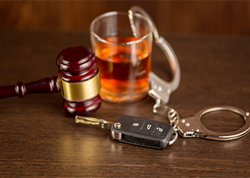 Glass of alcohol, handcuffs, car keys and gavel on table