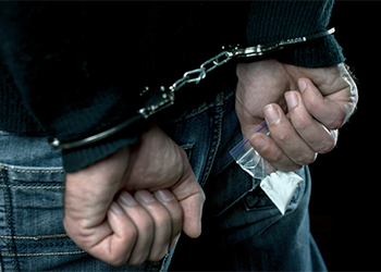 Man with handcuffs carrying pouch of drugs