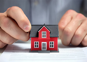 A person is placing a small red house on a document