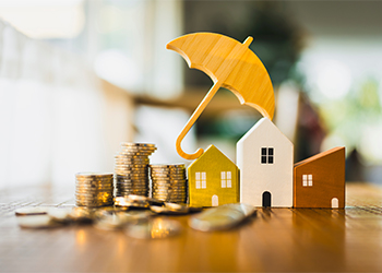House model and stack of coins protected by umbrella