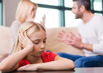 Sad little girl with arguing parents in background