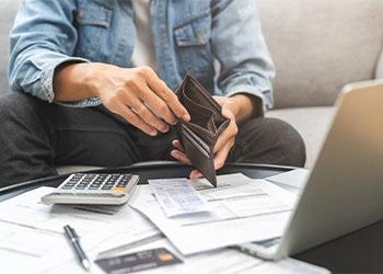 Man with unpaid bills on table and empty wallet in hand