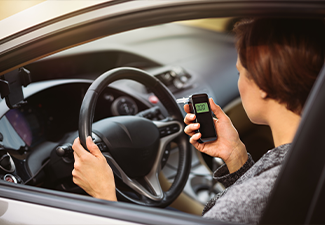 Young millennial woman using breath alcohol analyzer in the car