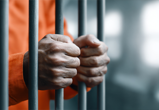 Close-up of elderly man gripping jail cell bars with hands