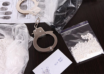 Drugs on table with handcuff and criminal fingerprint