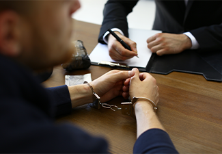 Police officer interrogating criminal in handcuffs at desk indoors