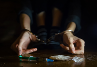 Syringe and drugs with a defocused man sitting on the floor