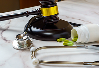 Wooden judge's hammer next to a pack of pills and a stethoscope on a table