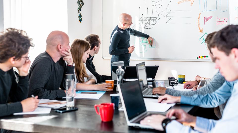 A presenter explains key points at a whiteboard while other employees take notes.
