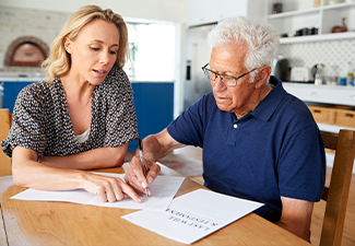 Woman Helping Senior Man To Complete Last Will And Testament At Home