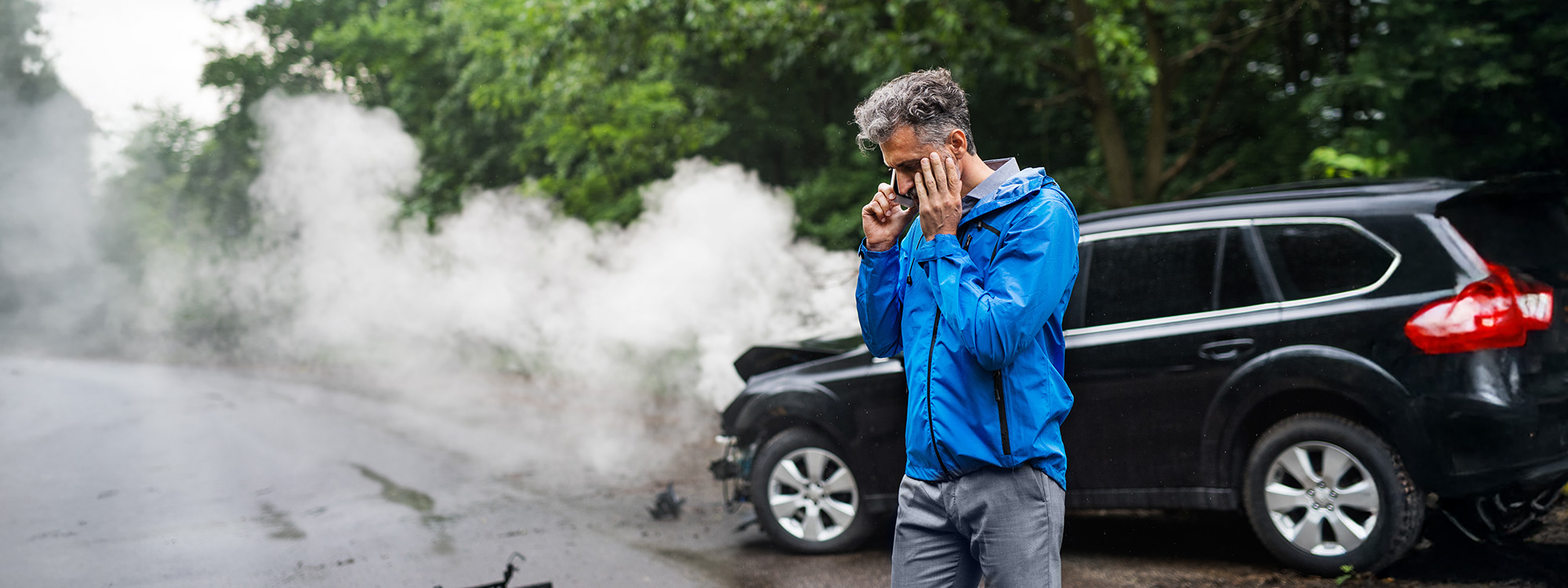 A man on the phone, while his wrecked car is smoking