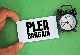 An alarm clock and a hand holding a white paper with the words plea bargain
