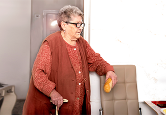 A sweet grandmother with a stick waits for breakfast with a loaf of bread in her hand at a nursing home