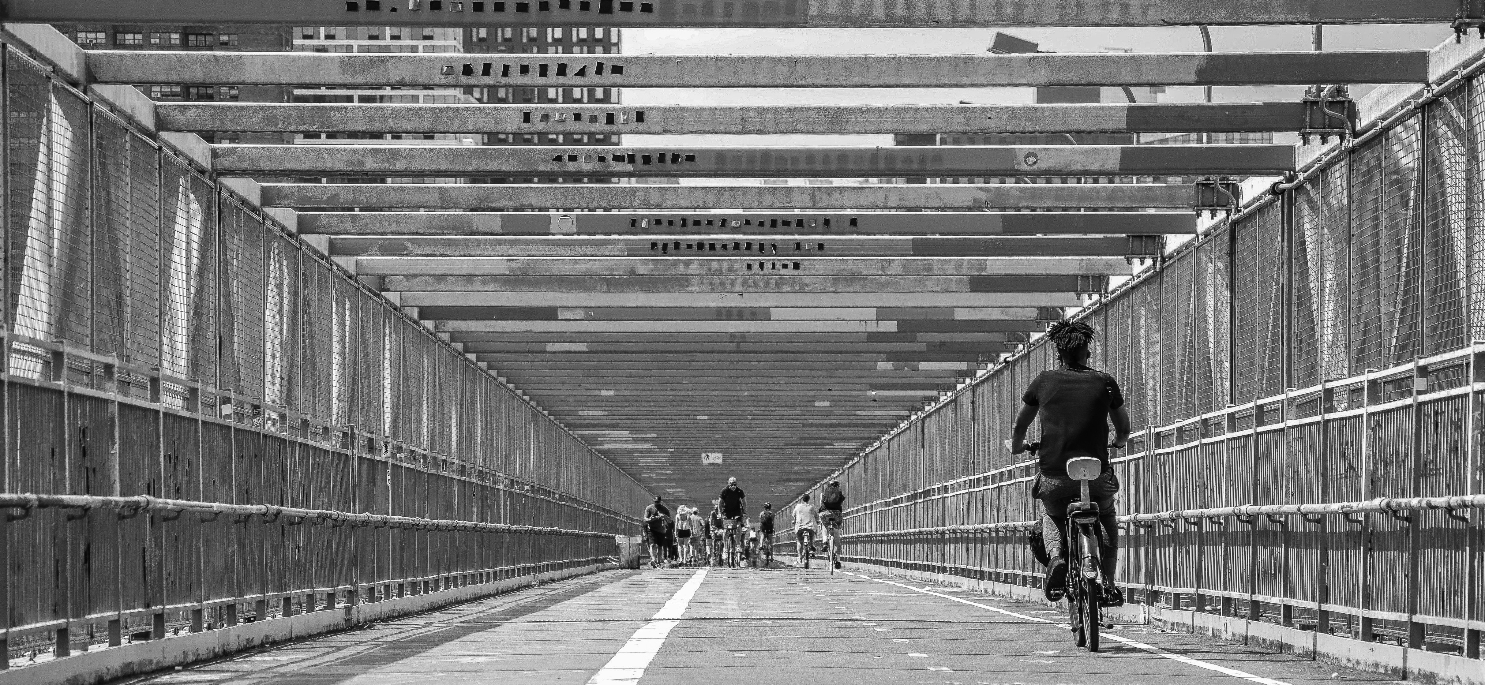 Solo bike rider on New York City bridge heading toward a group of cyclists