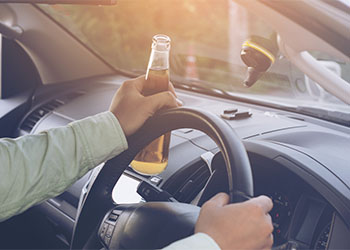 Man driving car with bottle of alcohol on hand