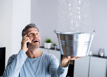 Man holding bucket to collect leaked water from celling