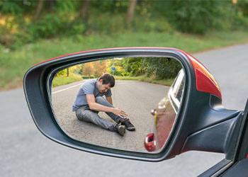 Injured man on road seen on side view mirror of a car