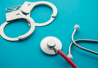 Handcuffs and stethoscope on blue background