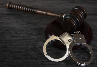 Handcuffs and gavel on dark rustic table