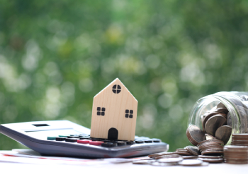 House model on calculator with stack of coins