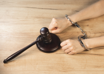 Handcuffed hands of man and gavel on table