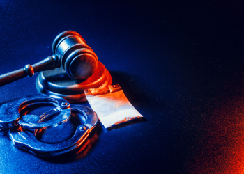 Gavel, handcuffs and pouch of drug on table