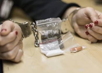 Handcuffed hands with drugs in table