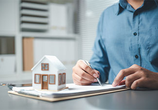A professional signing real estate documents beside a small house model
