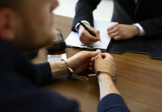 Police officer interrogating criminal in handcuffs at desk indoors