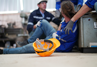 Worker receiving industrial injury in factory and colleague helping him while injured on leg